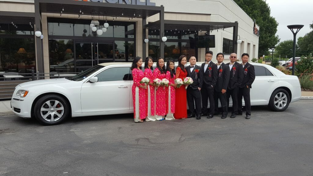 Bridal party with bride in groom in front of white limo during the day