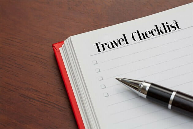 A book with the words Travel Checklist written with bullet points and a pen on top